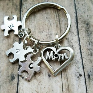 May include: Silver keychain with a heart charm that says "Mom" and three puzzle piece charms with the letters "M", "N", and "C".