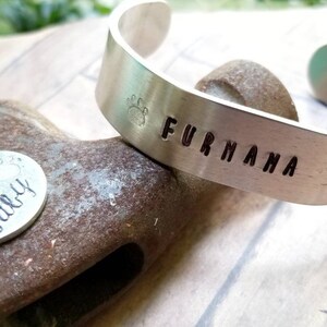 Könnte beinhalten: Silberarmband mit den Worten "Fur Mama" und einem eingeprägten Pfotenabdruck. Ein silberner Schlüsselanhänger mit den Worten "Fur baby" und einem Pfotenabdruck ist ebenfalls abgebildet.