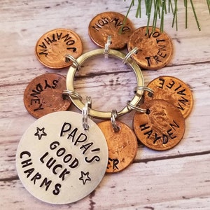 May include: A silver keychain with the words "Papa's Good Luck Charms" and a star on each side. The keychain has seven copper pennies attached to it, each with a name engraved on it: Hayden, Trent, Sydney, Jonathan, Dawson, Annie, and Tyler.