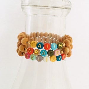 May include: Three wooden bead bracelets with the words "FAITH", "GRACE", and "BELIEVE" spelled out in colorful beads with gold lettering.
