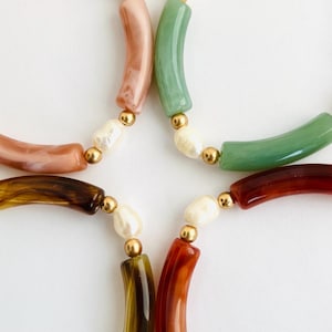 May include: A multi-colored beaded necklace with curved, colorful beads and white pearl accents. The necklace features a variety of colors, including brown, green, orange, and pink.