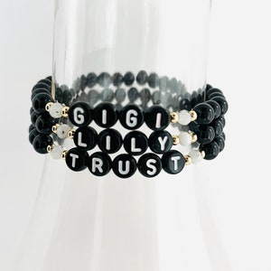 May include: Three black beaded bracelets with white letters spelling out "GIGI LILY TRUST".