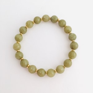 May include: A green gemstone bracelet with gold accents. The bracelet is made of round beads and is strung on a clear elastic cord.