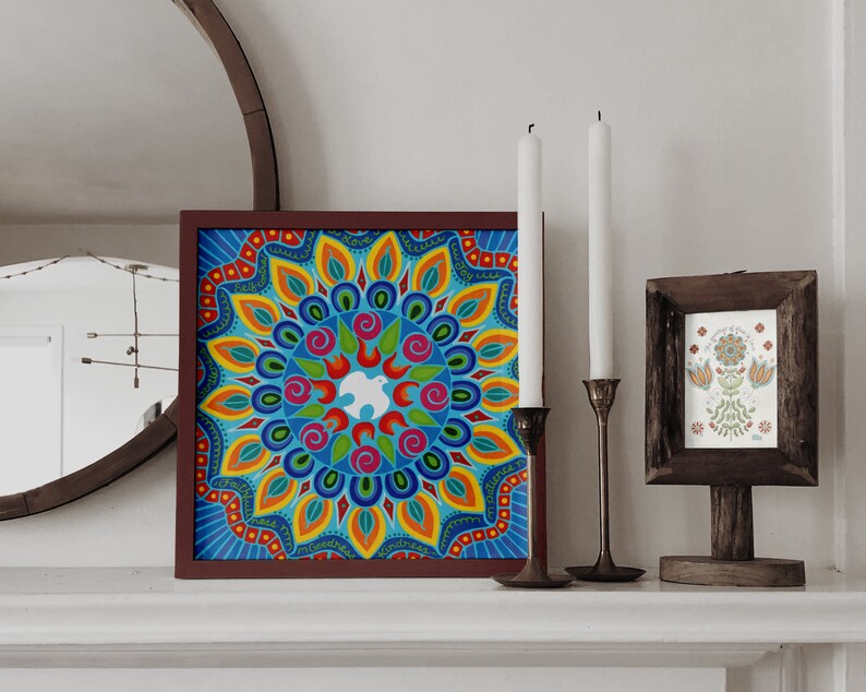 May include: A framed colorful mandala artwork with a white dove in the center. The mandala is surrounded by a border of text that reads "This is my masterpiece, kindness is my masterpiece". The artwork is hanging on a white wall with two candlesticks and a framed print of a floral design.