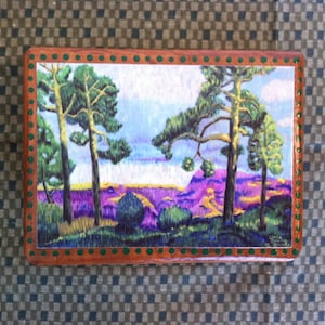 May include: A wooden box with a painted scene of a purple mountain range with three green trees in the foreground. The box has a green and brown border.