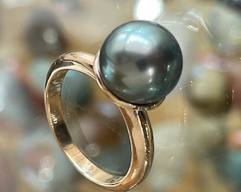 May include: A gold ring with a large, dark green pearl. The pearl is round and has a smooth, shiny surface.