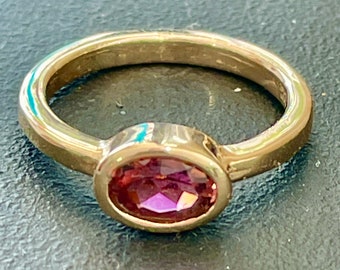 May include: A gold ring with a bezel set oval shaped purple gemstone.