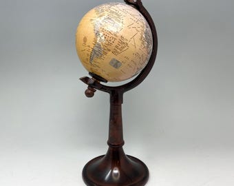 May include: A vintage-style globe with a cream-colored map, mounted on a dark brown wooden stand. The globe features geographical details and is supported by a curved frame. The base is round and the stand is a dark, rich brown.