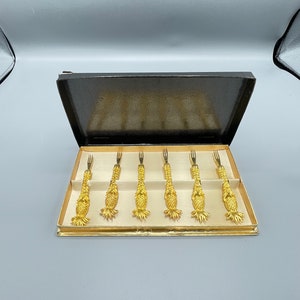 May include: Set of six gold-toned pineapple-shaped cocktail forks in a black box with a white interior.