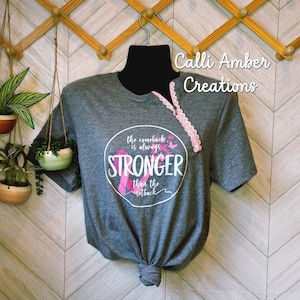 May include: A grey t-shirt with a round graphic that says "the comeback is always STRONGER than the setback" with a pink ribbon and butterflies. The shirt has a pink lace trim and is knotted at the bottom.