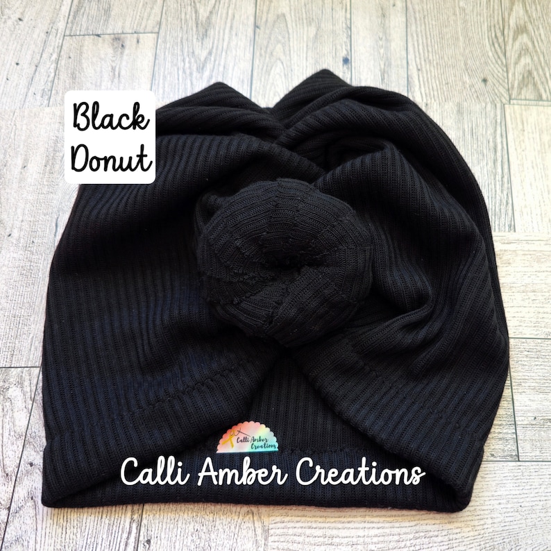 Op de afbeelding: Een zwarte tulband van geribbelde stof met een centraal geknoopt donut-detail. De tekst Black Donut staat in de linkerbovenhoek en de tekst Calli Amber Creations staat onderaan met een klein kleurrijk logo.
