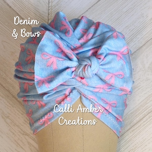 Puede incluir: Un turbante azul claro con estampado de mezclilla y detalles de lazos rosas. El turbante presenta el texto "Denim & Bows" y "Calli Amber Creations". El turbante se muestra en una cabeza de maniquí.