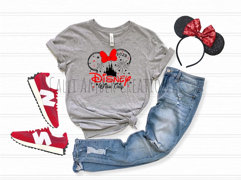 May include: A gray t-shirt with a black and red graphic of Mickey Mouse ears with a bow, fireworks, and the text "Disney Wish Trip 2023". The shirt is paired with blue jeans, red sneakers, and a black headband with red glitter ears.