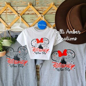 May include: Three gray and white t-shirts with a black and red Mickey Mouse ears design. The shirts have the text "2024 Disney Wish Trip" on them. The shirts are hanging on a wooden rack with a brown hat on top.