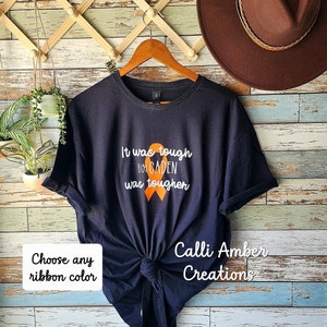 May include: Black t-shirt with the text "It was tough but CADEN was tougher" and an orange ribbon. The text "Calli Amber Creations" is also on the shirt. Choose any ribbon colour.