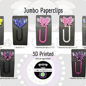 Pode incluir: Uma coleção de clipes de papel jumbo com vários designs, incluindo uma abelha, um coração com a frase "Be Kind", laços de coração, uma vaca das Terras Altas e laços de caveira. Cada clipe está preso a um cartão preto. O texto "Jumbo Paperclips" e "3D Printed" também é visível.