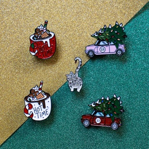 Op de afbeelding: Set van vijf emaillepins met een mok met warme chocolademelk, een kat, een auto met een kerstboom op het dak en twee auto's met kerstbomen op het dak. De pins zijn allemaal in verschillende kleuren en hebben een feestelijk kerstthema.