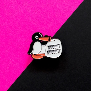 Op de afbeelding: Een zwart-witte emaille speld met een cartoonpinguïn met een oranje snavel en voeten. De pinguïn houdt een witte tekstballon vast met de zwarte tekst "NOOOOT NOOOOT!" in een vetgedrukt, schreefloos lettertype.