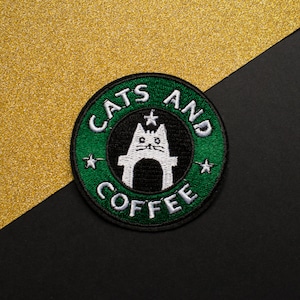 Puede incluir: Parche bordado verde y blanco con el texto "Cats and Coffee" y una silueta de gato blanco dentro de un círculo.