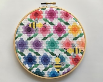 May include: A colorful embroidery hoop with a pattern of flowers and bees. The flowers are in shades of pink, purple, blue, yellow, and orange. The bees are yellow with black stripes.