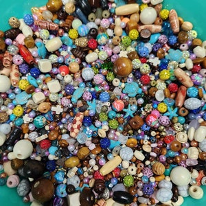 May include: A large bowl filled with a variety of colourful beads. The beads are made of wood, glass, and plastic. There are many different shapes and sizes of beads, including round, square, and star-shaped beads.