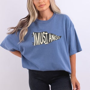 May include: A blue t-shirt with a vintage-style pennant graphic that says "MUSTANGS" in white lettering.