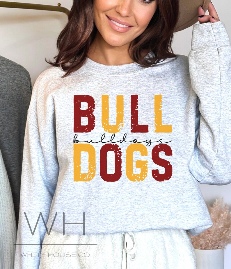 Puede incluir: Una sudadera gris con las palabras "BULLDOGS" en letras rojas y amarillas con un aspecto desgastado. El texto "WH WHITE HOUSE CO" est&aacute; en la parte inferior de la sudadera.