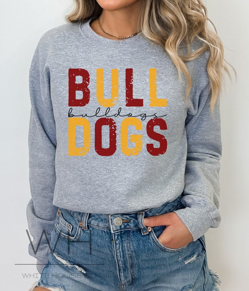 Puede incluir: Sudadera gris con un dise&ntilde;o gr&aacute;fico desgastado que dice "BULLDOGS" en letras rojas y amarillas.
