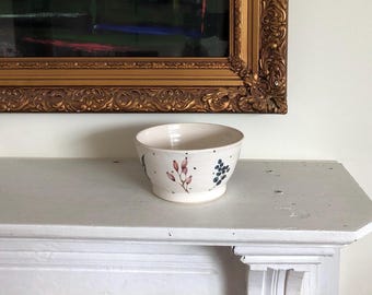 May include: A white ceramic bowl with a floral design. The bowl has pink and blue flowers and black dots.