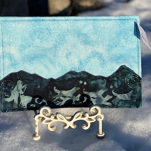 May include: A blue and green fabric placemat with a mountain range and stars design. The placemat is on a white stand.