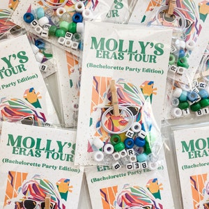 May include: Clear plastic bags containing beads, white string, and wooden clothespins. Each bag has a card with the text "MOLLY'S ERAS TOUR (Bachelorette Party Edition)" and a colorful graphic of a woman.