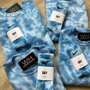 May include: Four tie-dye shirts and four pairs of tie-dye socks. The shirts and socks are all in shades of blue and white. The shirts have the text "WH WHITE HOUSE CO" on the tag. The socks have the text "SKY WH" on the tag.