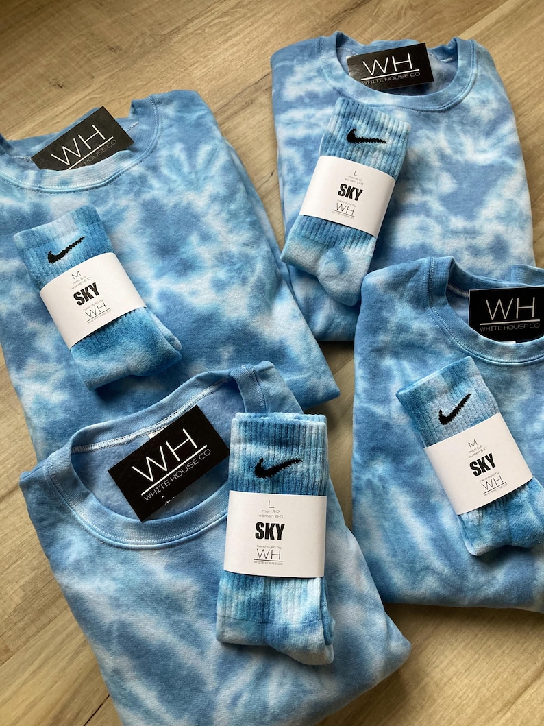May include: Four tie-dye shirts and four pairs of tie-dye socks. The shirts and socks are all in shades of blue and white. The shirts have the text "WH WHITE HOUSE CO" on the tag. The socks have the text "SKY WH" on the tag.