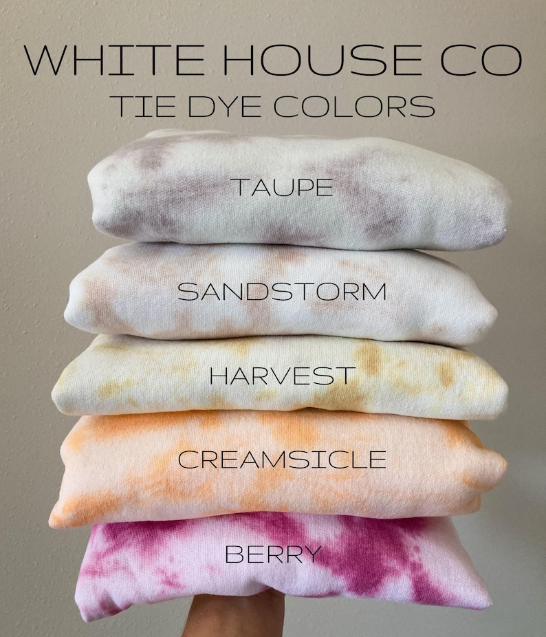 May include: A stack of five tie-dye sweatshirts in different colours, including taupe, sandstorm, harvest, creamsicle, and berry. The sweatshirts are folded and stacked on top of each other. The text "WHITE HOUSE CO TIE DYE COLORS" is at the top of the image.