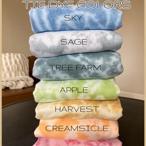 May include: A stack of tie-dye fabric swatches in various colours, including sky blue, sage green, tree farm green, apple green, harvest orange, creamsicle orange, and berry pink. The fabric swatches are labelled with the colour names.