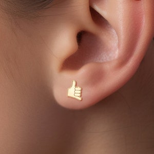 Puede incluir: Un par de pendientes de oro, uno con forma de pulgar hacia arriba y el otro con forma de ojo malvado con diamantes.