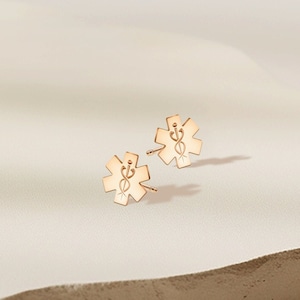 May include: A pair of gold-toned stud earrings featuring a medical symbol, the Star of Life, with a snake and staff design.
