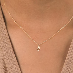 Puede incluir: Un collar de cadena de oro con un pequeño colgante delicado. El colgante tiene la forma de una mano con los dedos entrelazados.