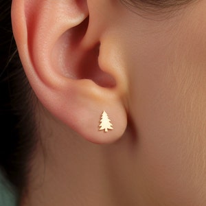 May include: A close-up of a person's ear with a small gold tree-shaped stud earring.