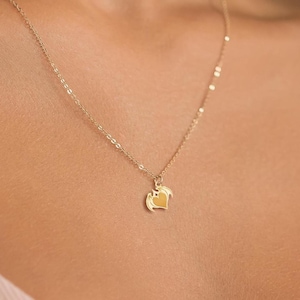 Könnte beinhalten: Eine zarte goldene Halskette mit einem herzförmigen Anhänger. Der Anhänger hat eine strukturierte Oberfläche und hängt an einer feinen Kette. Die Halskette wird um den Hals getragen und zeigt ihr elegantes Design und ihren subtilen Glanz.
