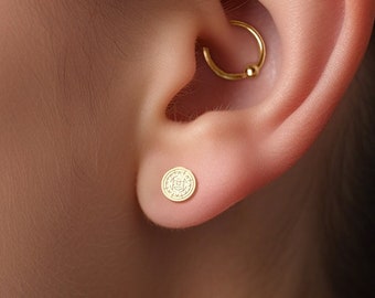 May include: Gold hoop earring with a small ball charm and a gold stud earring with a circular design.