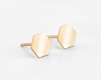 Può includere: Un paio di orecchini a bottone esagonali in oro. Gli orecchini sono piccoli e semplici, il che li rende un accessorio versatile per ogni occasione.