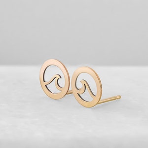 May include: A pair of gold-toned earrings with a wave design. The earrings are circular and have a cut-out wave shape.