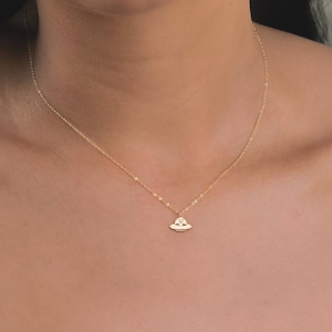 May include: A gold chain necklace with a small, delicate pendant shaped like a flying saucer. The pendant has a small circle in the center.