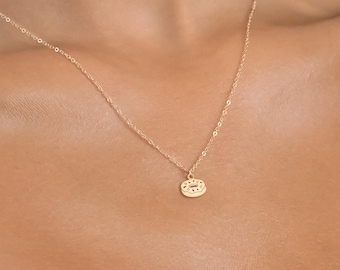 Könnte beinhalten: Eine goldene Kettenkette mit einem kleinen, runden Anhänger mit strukturiertem Design.