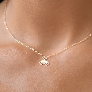 Könnte beinhalten: Eine zarte goldene Kettenkette mit einem kleinen, filigranen Schmetterlingsanhänger.