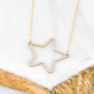 May include: A gold-toned necklace with a simple, open star pendant. The necklace is displayed on a white marble surface.
