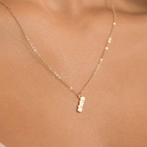 Puede incluir: Un delicado collar de oro con un pequeño colgante rectangular. El colgante está suspendido de una fina cadena, creando un diseño minimalista y elegante. El collar es de color oro cálido y se lleva alrededor del cuello.