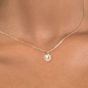 以下が含まれることがあります： 小さな太陽と月のペンダントが付いたゴールドチェーンネックレス。ペンダントは三日月と太陽の光線で詳細に描かれています。