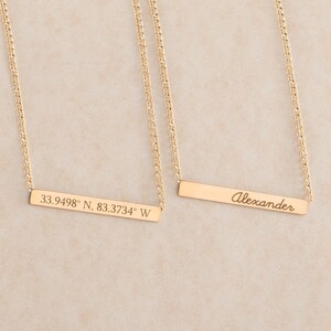 May include: Two gold necklaces with bar pendants. One pendant is engraved with the coordinates "33.9498&deg; N, 83.3734&deg; W". The other pendant is engraved with the name "Alexander".